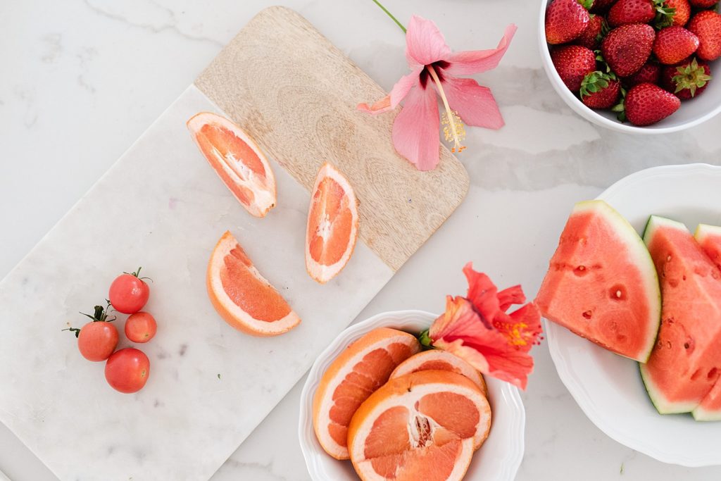 Cherry tomatoes and orange slices on a chopping board, oranges, and watermelon slices on a plate, and strawberries on a bowl.