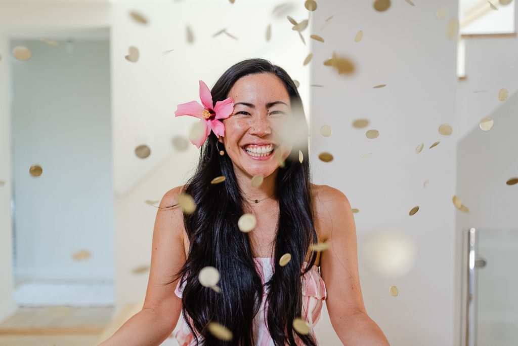 Woman smiling with a pink flower on her hair. Confetti is falling around her.