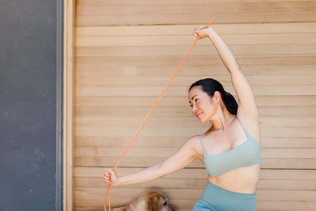 Woman in workout clothes is pulling a rope taut while leaning to her side.