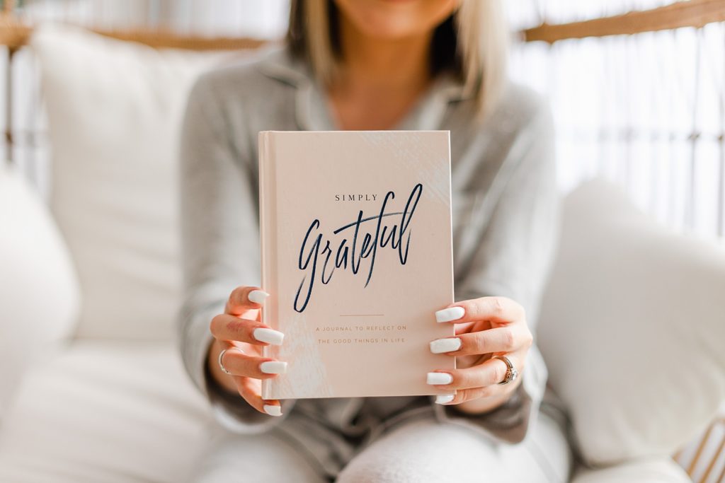 Woman holding up a book with the title 'Simply Grateful'.