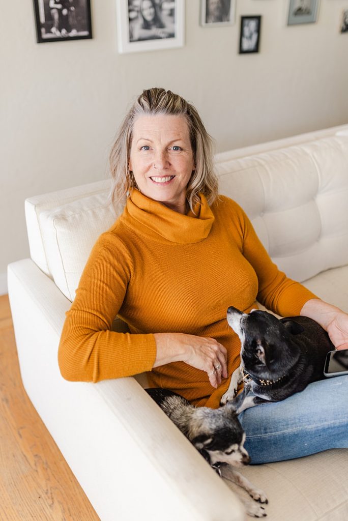woman in orange turtleneck sweater lounging on a white couch with a small pet dog on her lap