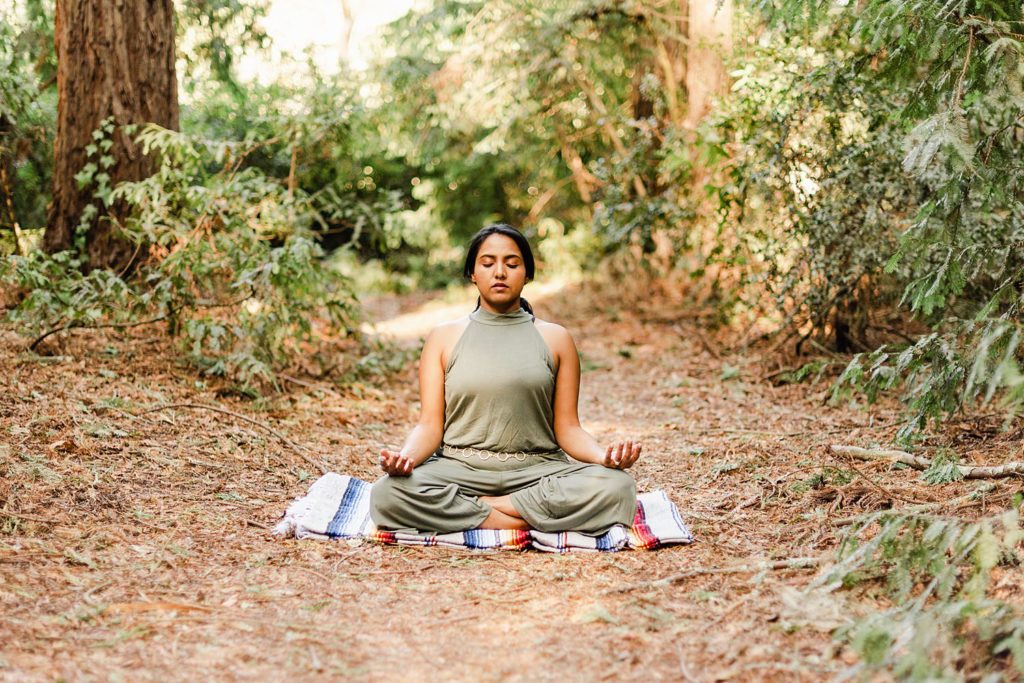 woman facing the camera sitting on the forest floor while meditating