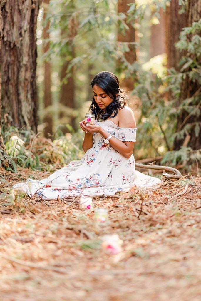 woman in a white dress sitting on the forest floor holding a candle on a glass