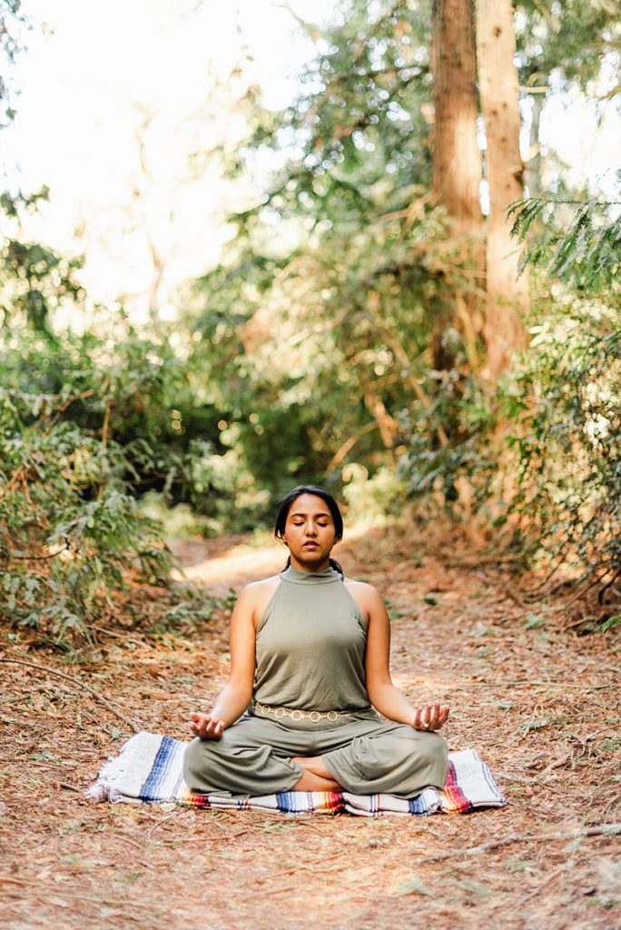 meditating woman sitting with her legs crossed on the forest floor