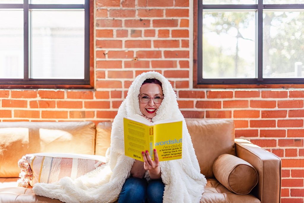 woman holding a yellow book called "wordslut" is covering herself with a white fluffy blanket