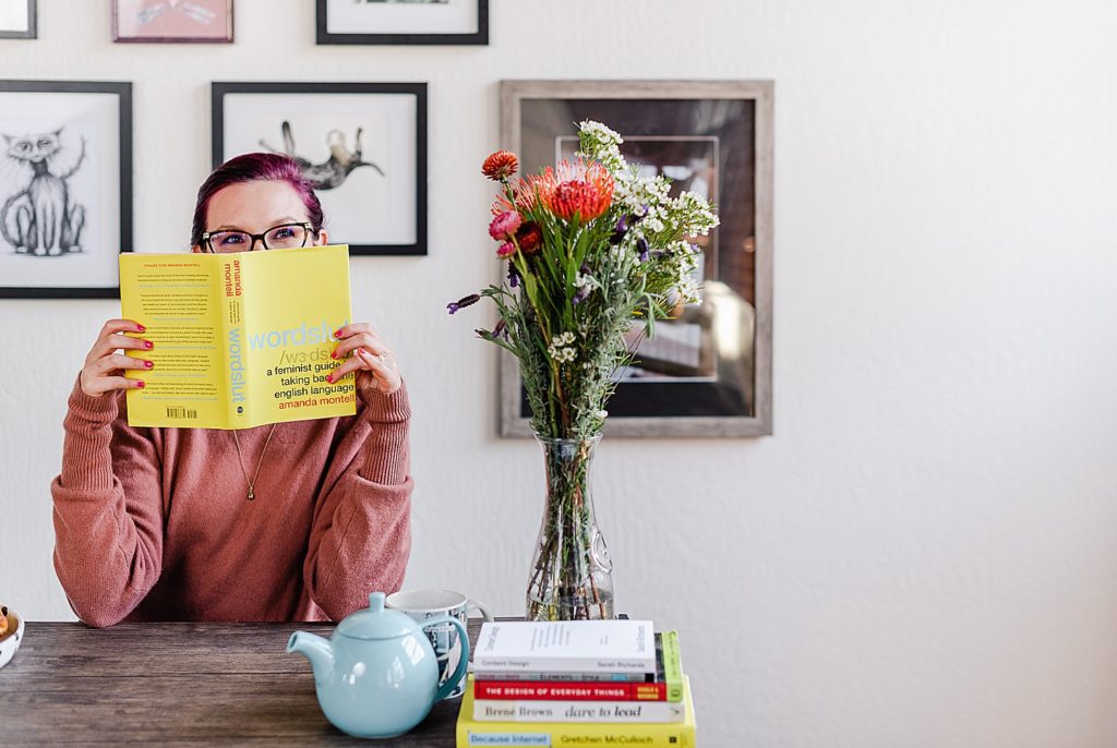 woman is peeking over a book called "wordslut". there's a vase filled with various flowers to her right.