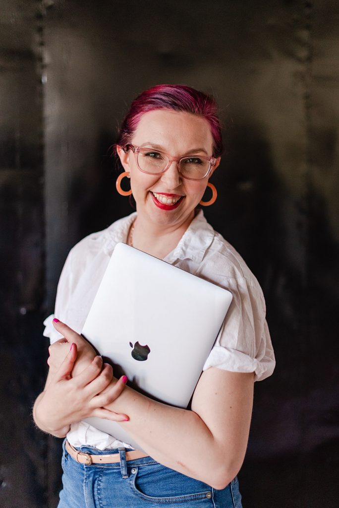 woman wearing glasses is hugging her macbook and smiling to the camera