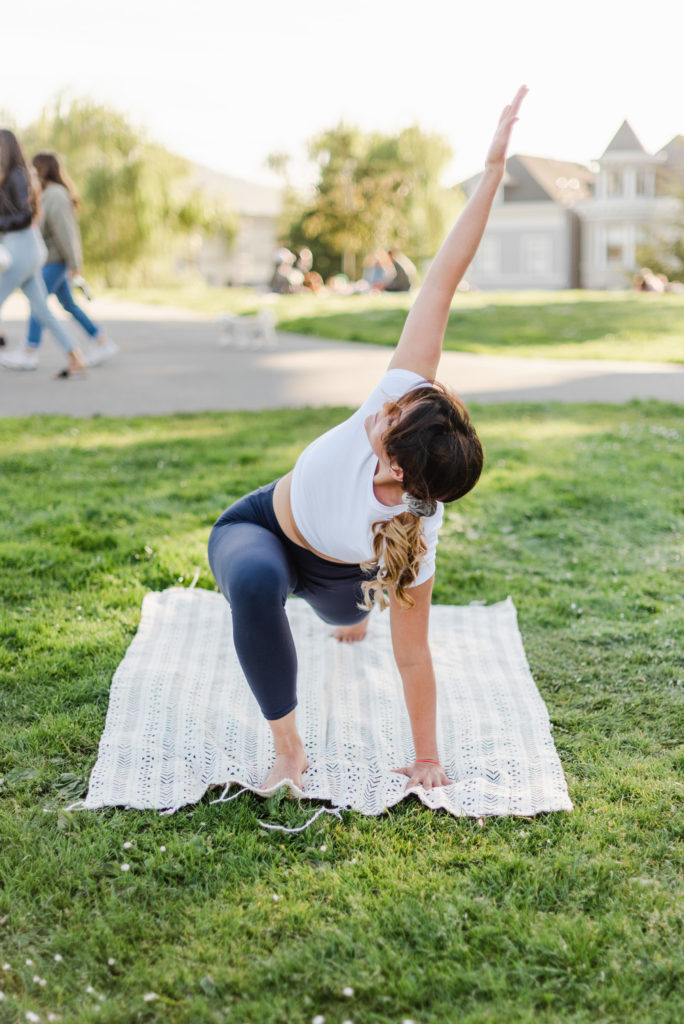 woman doing a triangle yoga pose on a white blanket on grass