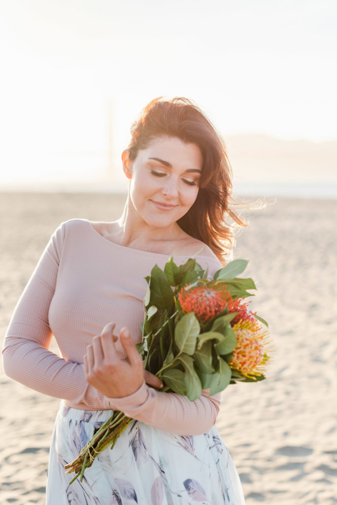 woman has a bouquet of flowers on her arms. she is looking down at the flowers while smiling