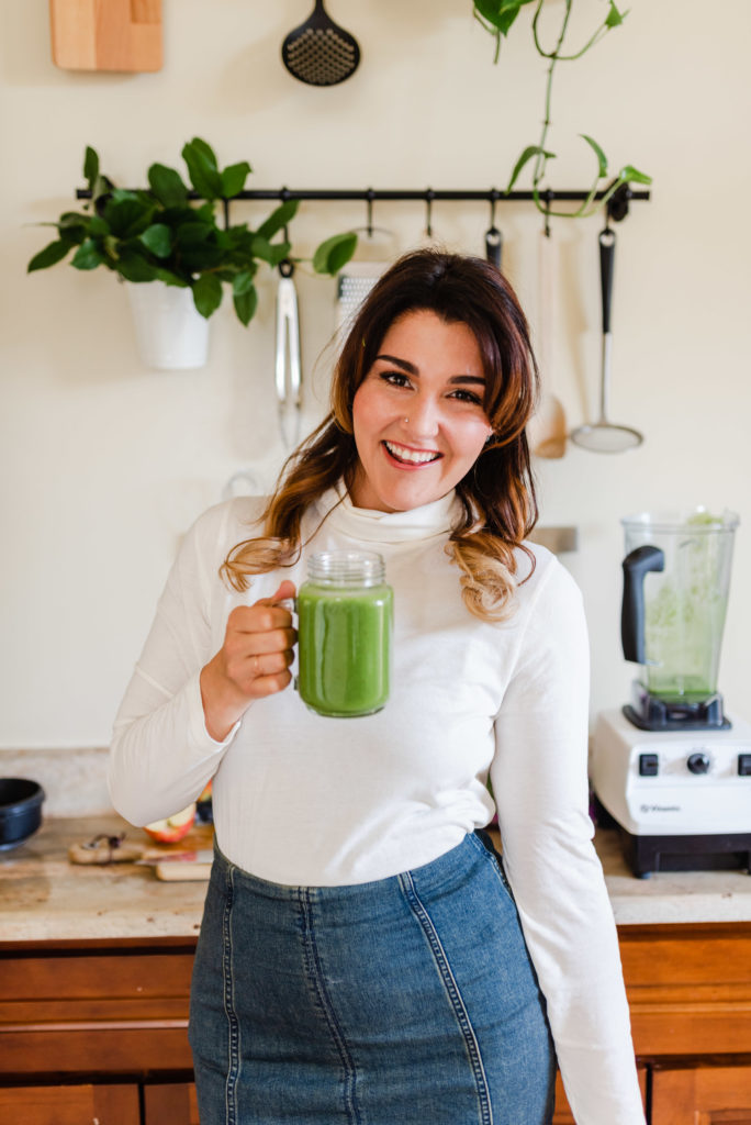woman holding a mug of green drink while smiling