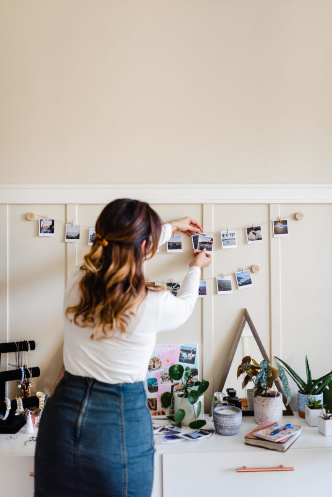 woman putting a polaroid on a string on the wall using a small wooden clip