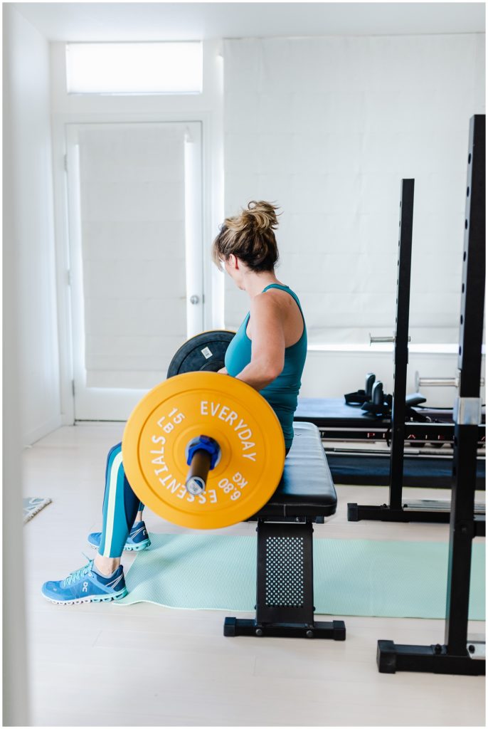 woman in workout clothes sitting on a bench with 15 lb of weights