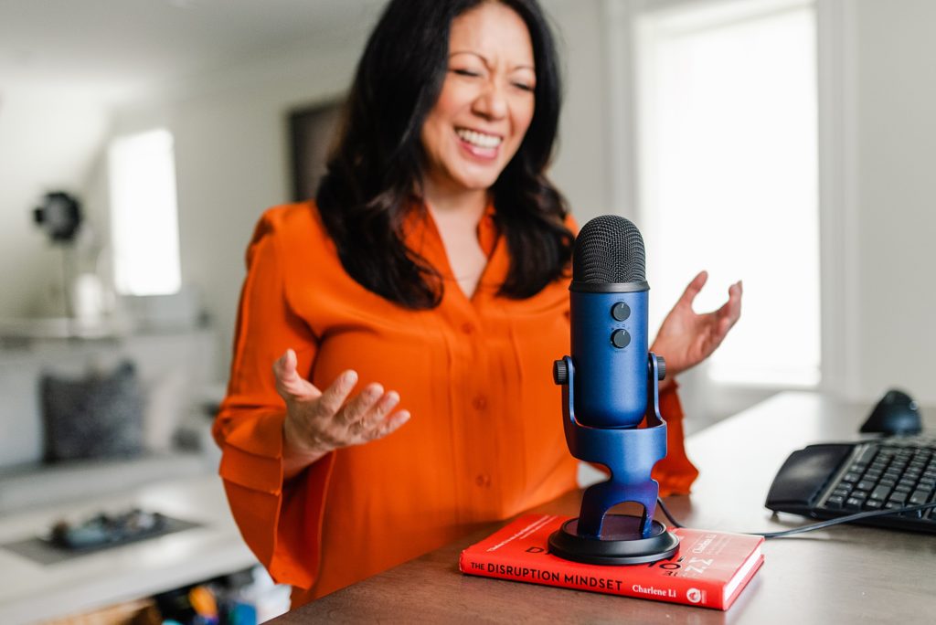 blue mic on top of a book on a wooden table with a woman behind it in the background smiling