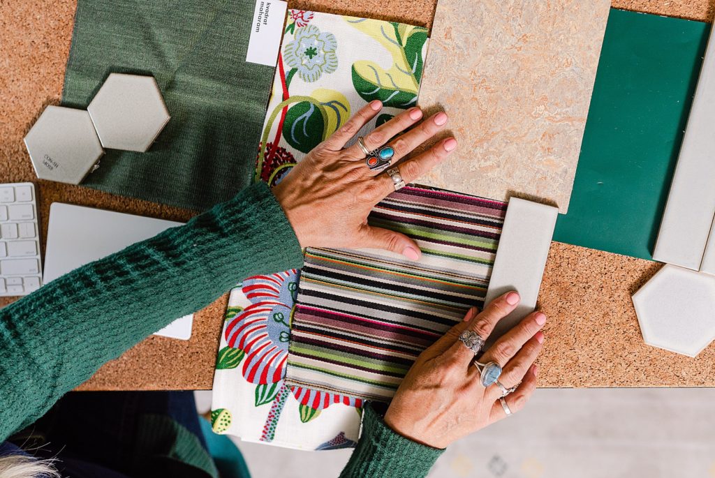 woman's hands arranging different samples of fabrics and tiles on top of a cork board