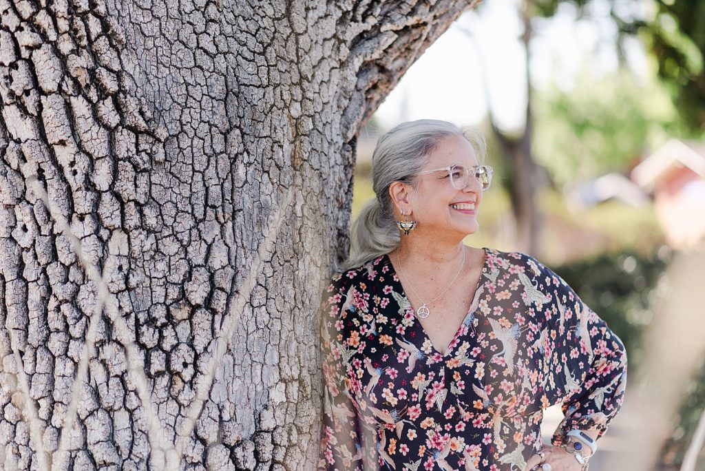 smiling woman in a floral blouse is leaning on a tree