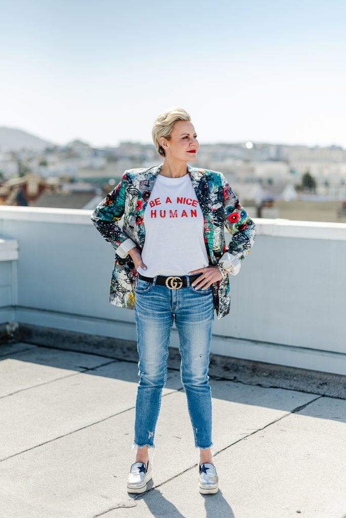 Woman wearing jeans and blazer with colorful print is standing with both her hands on her hips while looking to her side