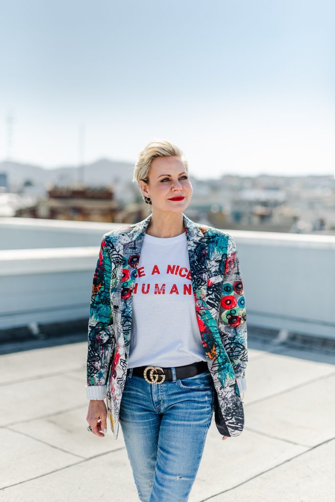 Woman wearing jeans and blazer with colorful print is standing looking off to the side