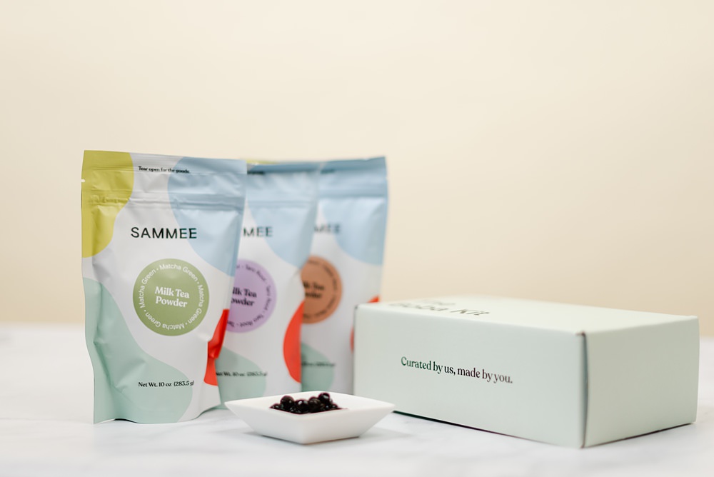 3 Sammee milk tea powder packs beside The Boba Kit box, and a saucer with cooked boba