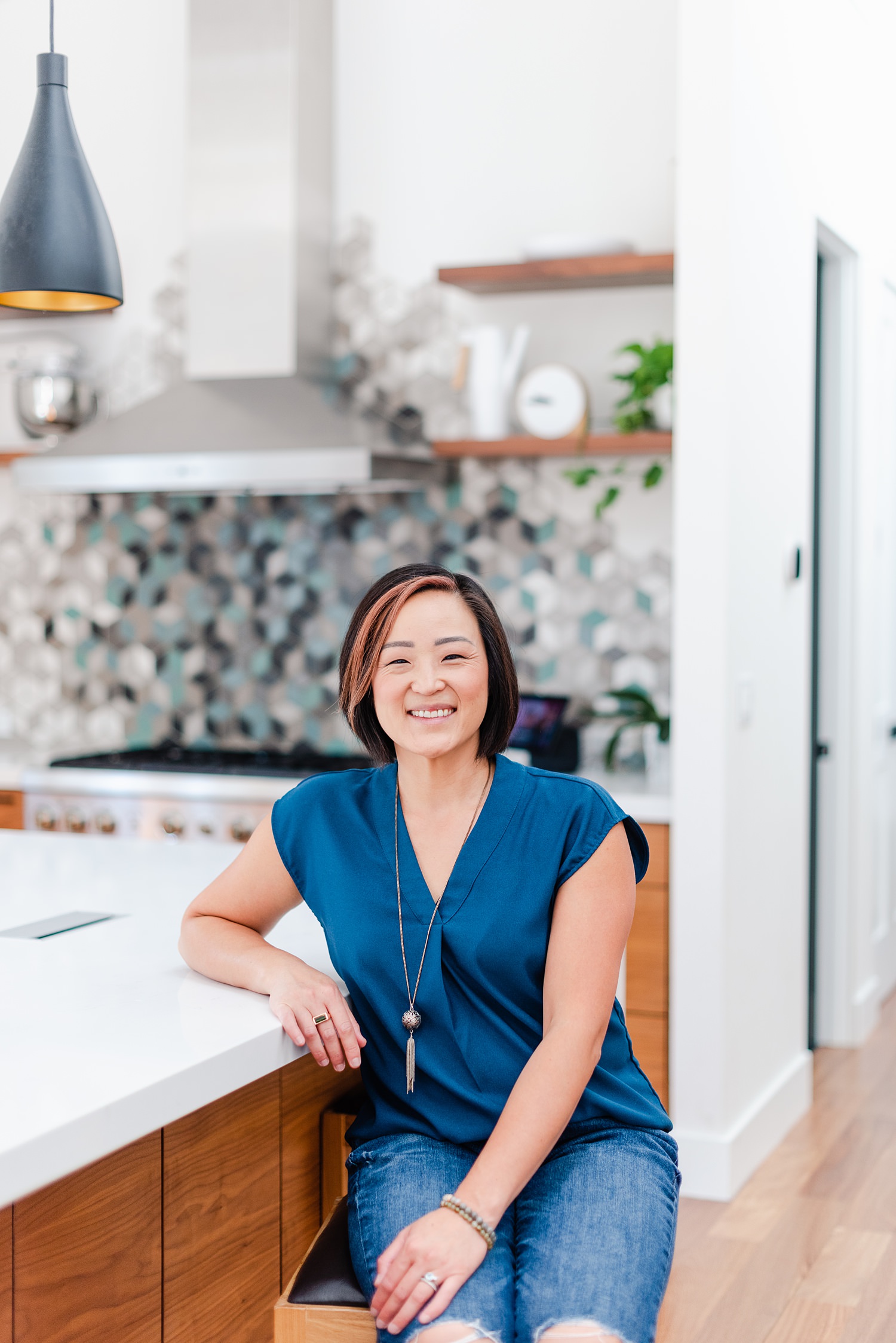 smiling woman wearing a blue blouse is sitting beside the kitchen counter