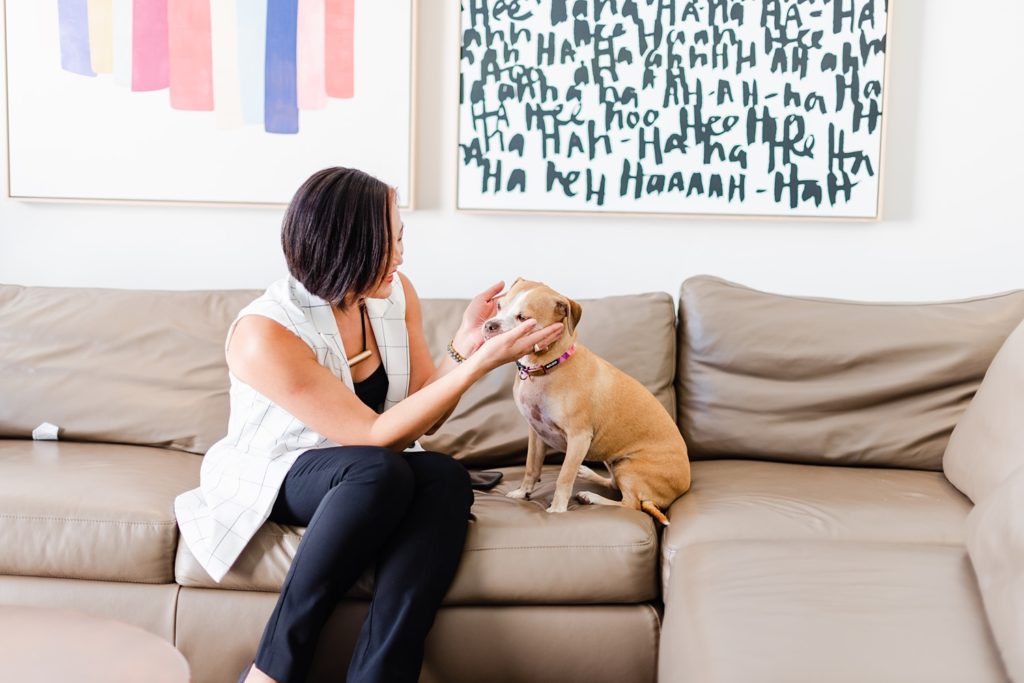 woman in a white vest is sitting on a cream colored leather sofa while playing with her dog
