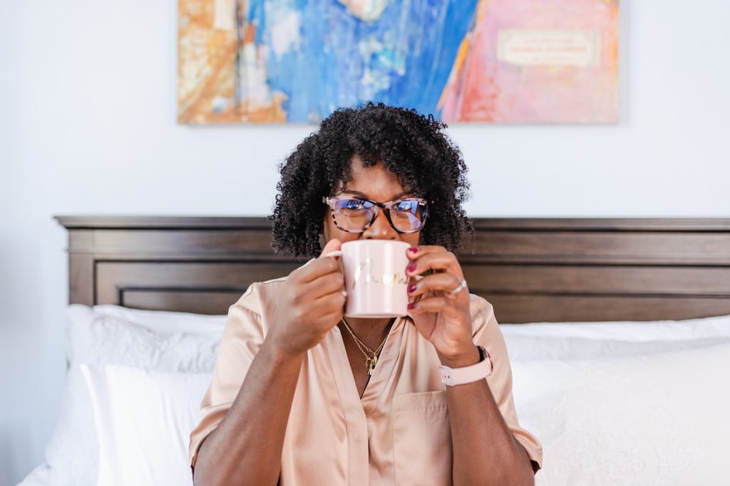 Woman wearing pink blouse sitting on a white sofa while drinking coffee