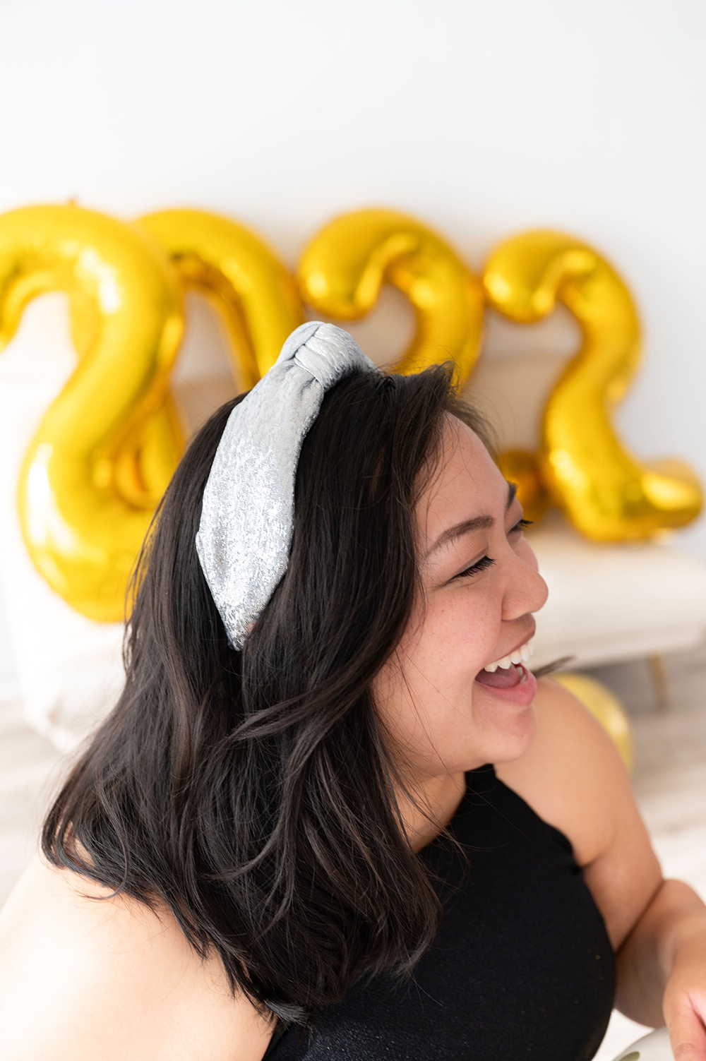 A smiling woman wearing a gold headband and celebrating new year 2022. She's looking to the right.