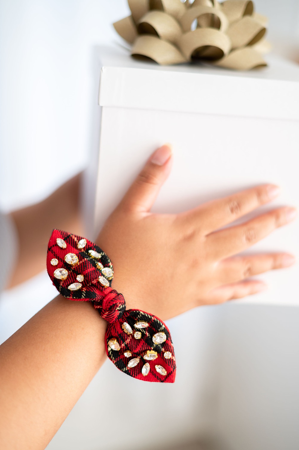Someone's hand wearing a checkered red ribbon while holding a while gift box.