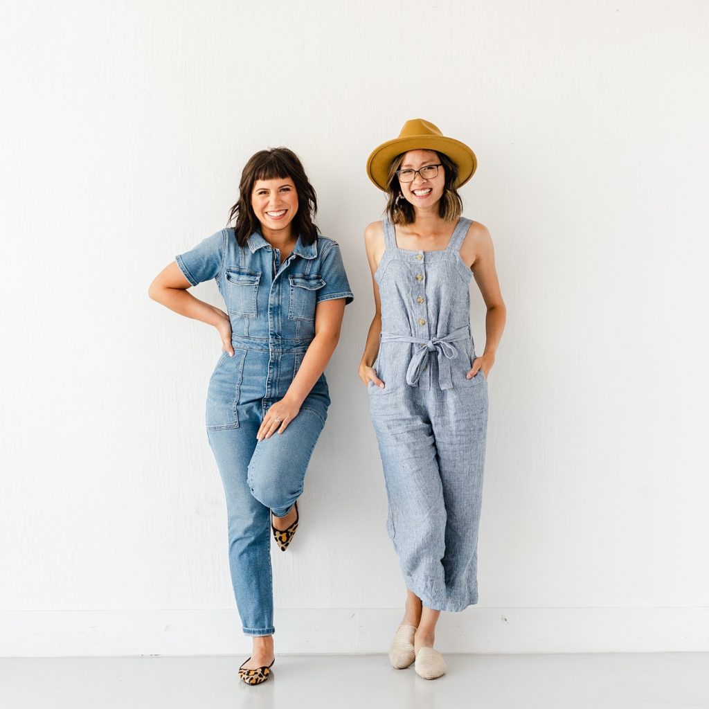 two women wearing blue jumpsuits standing against a white wall