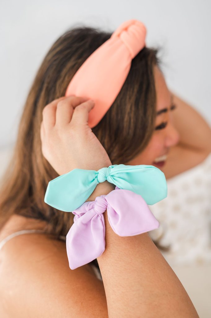 woman adjusting a peach colored headband. she has two neoprene scrunchies on her wrist.
