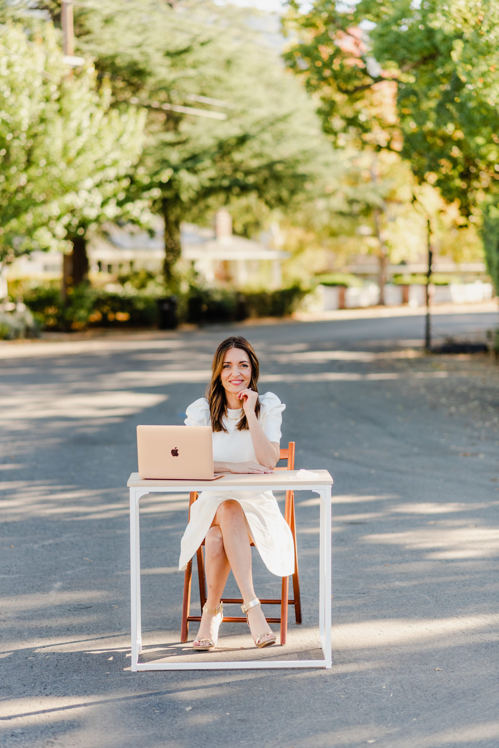 Real estate agent sitting on a desk with a laptop int he middle of the road with trees behind her