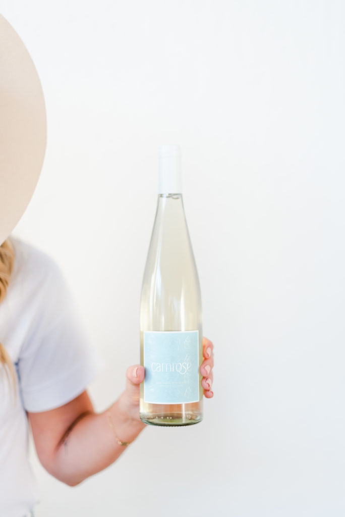 Woman in hat holding a bottle of wine, body cut off the side of photo